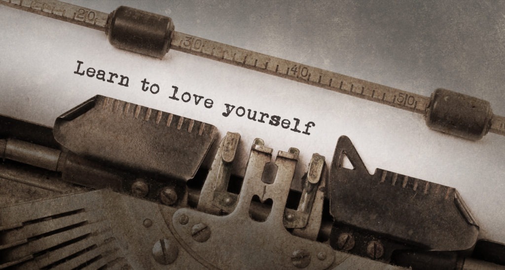 The words "learn to love yourself" are written on a vintage typewriter,