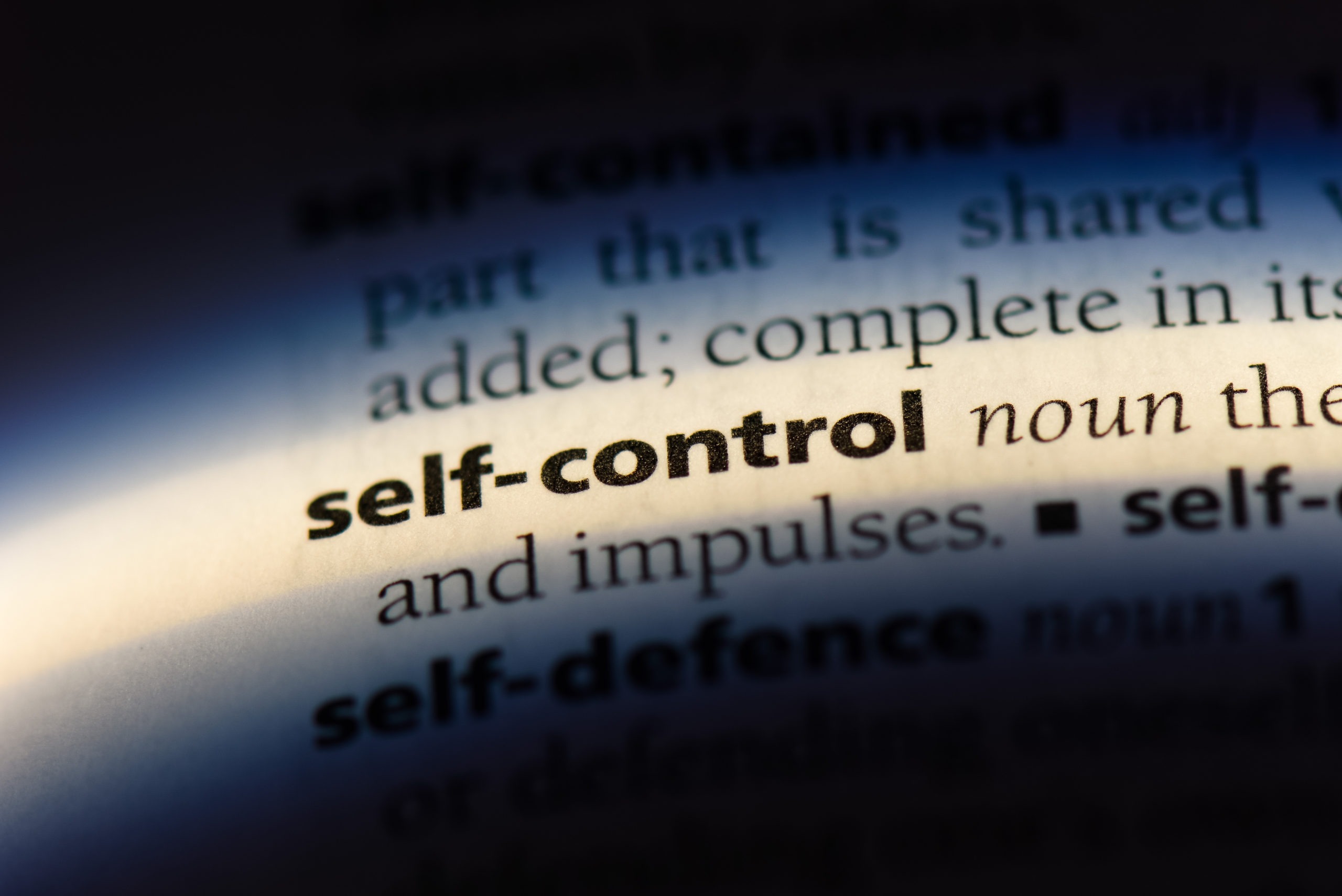 Zoomed in photo of the word "self-control noun" in a dictionary. The other surrounding words are in the dark. Self-control is essential for breaking bad habits.