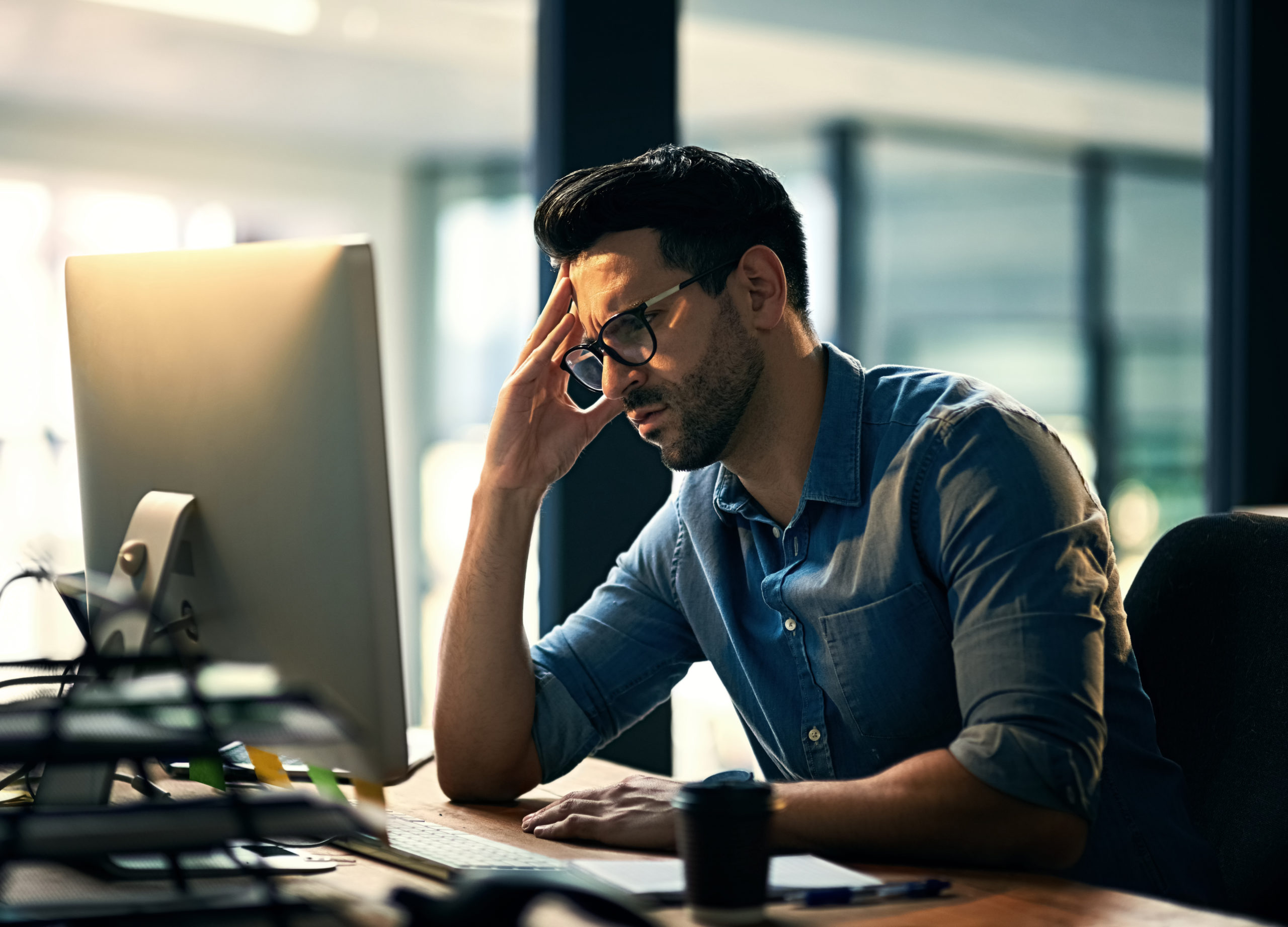 A man is staring at his computer with his hand against his head and an anxious look on his face. Overcoming entrepreneur depression is not easy, but there are ways to manage it.