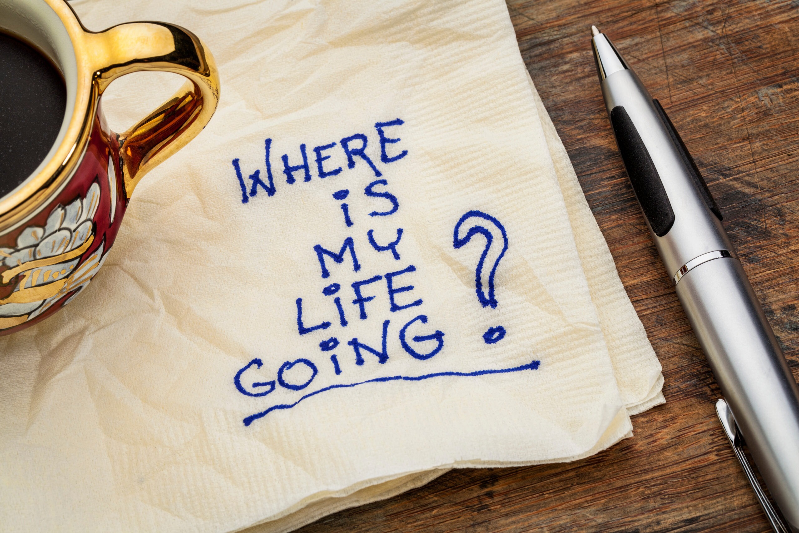 The words "where is my life going?" are written on a white napkin, next to a pen and gold mug. Your life purpose can change your life, but you have to figure it out first.