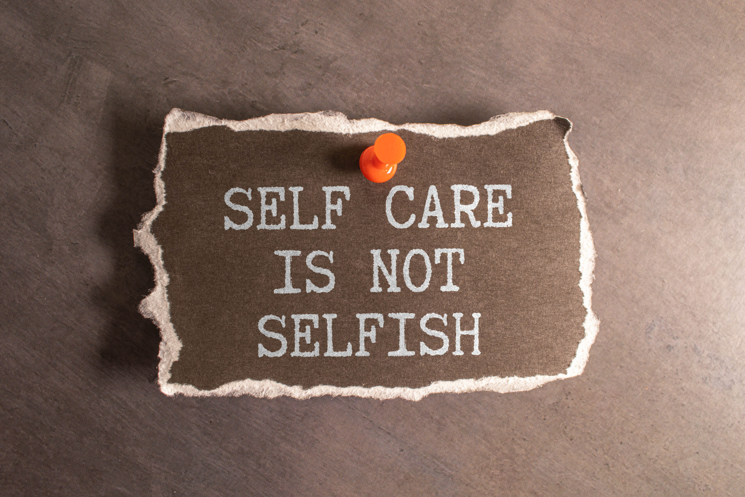 A piece of paper, clipped to the wall with an orange pin, reads "self care is not selfish". Feeling sorry for yourself is the opposite of self-care because you're not giving yourself power over your outcomes and well-being.
