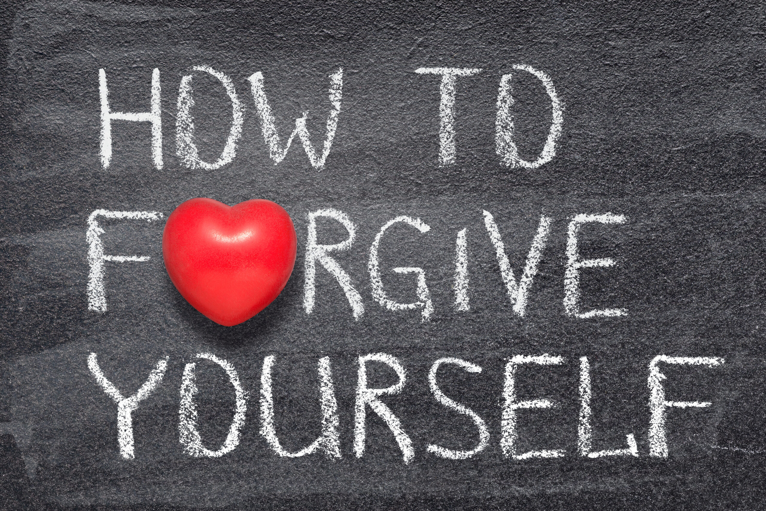 The words "how to forgive yourself" are written on a chalkboard, with a heart as the "o" in forgive yourself.