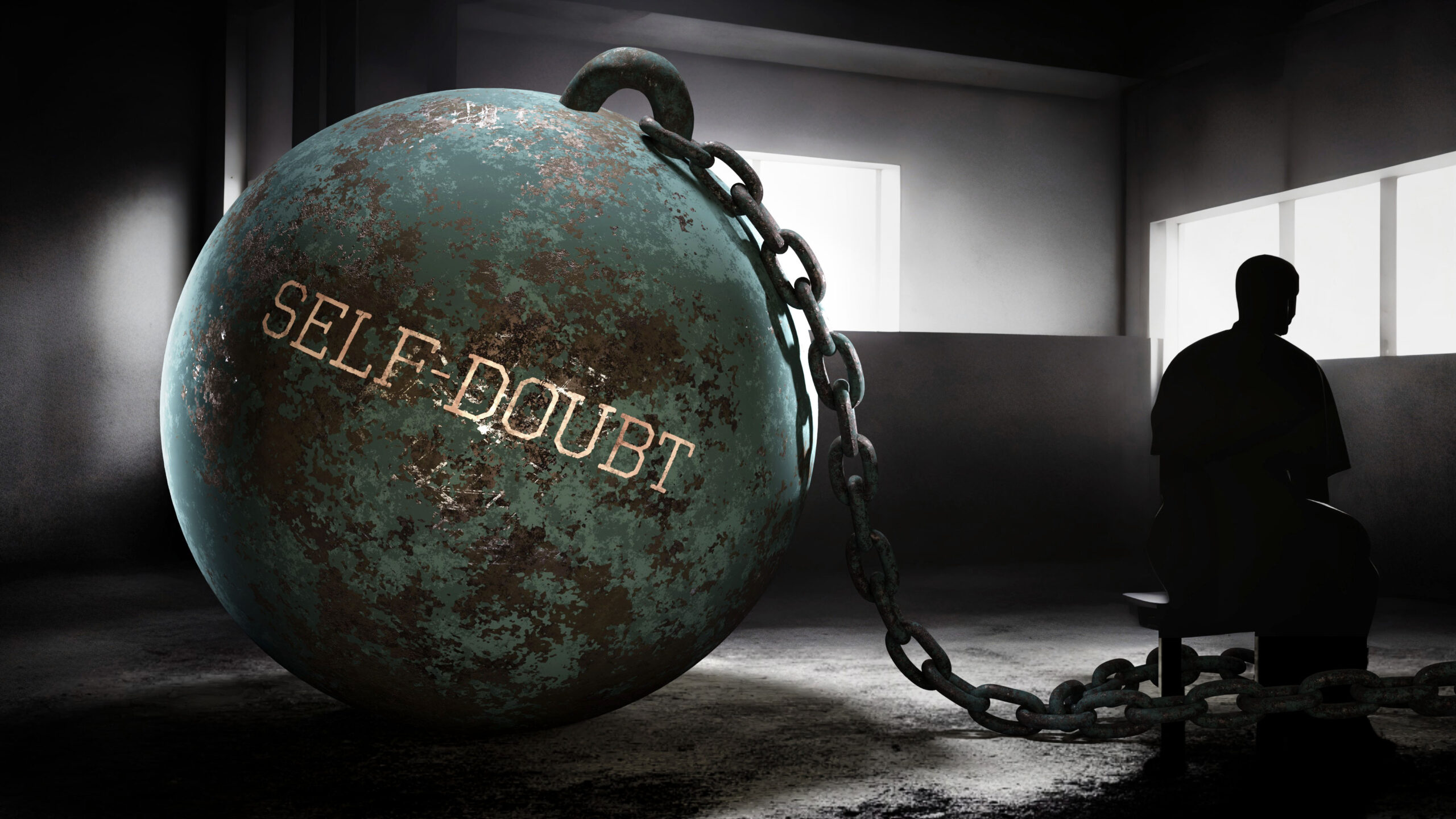 A man sits in a dark room, with a chain around his ankle that connects him to a giant ball. The words "self-doubt" are written on the ball.