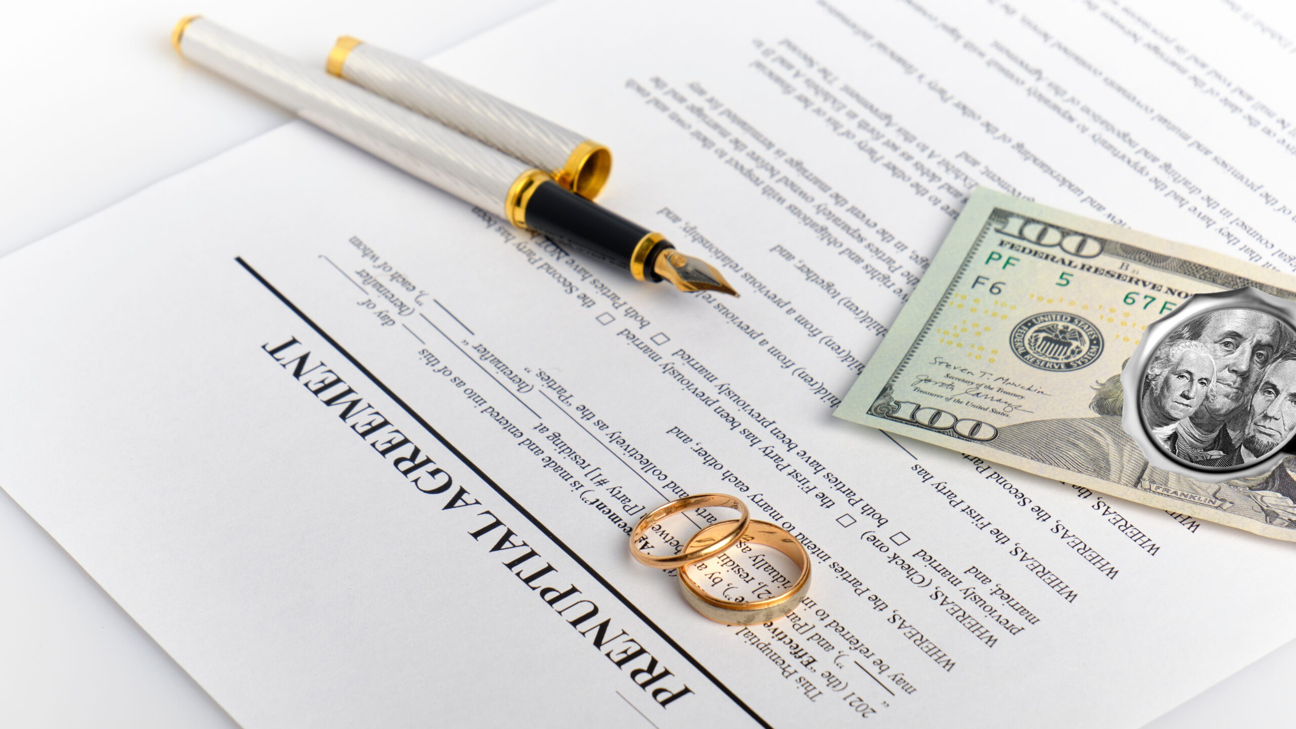 Two golden wedding rings, a pen, and money are sitting on top of a prenup agreement, which is one of the ways you can prevent money and relationship problems.