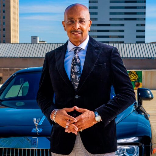 Dr. D Ivan Young standing in front of a black Rolls-Royce in a suit and tie.