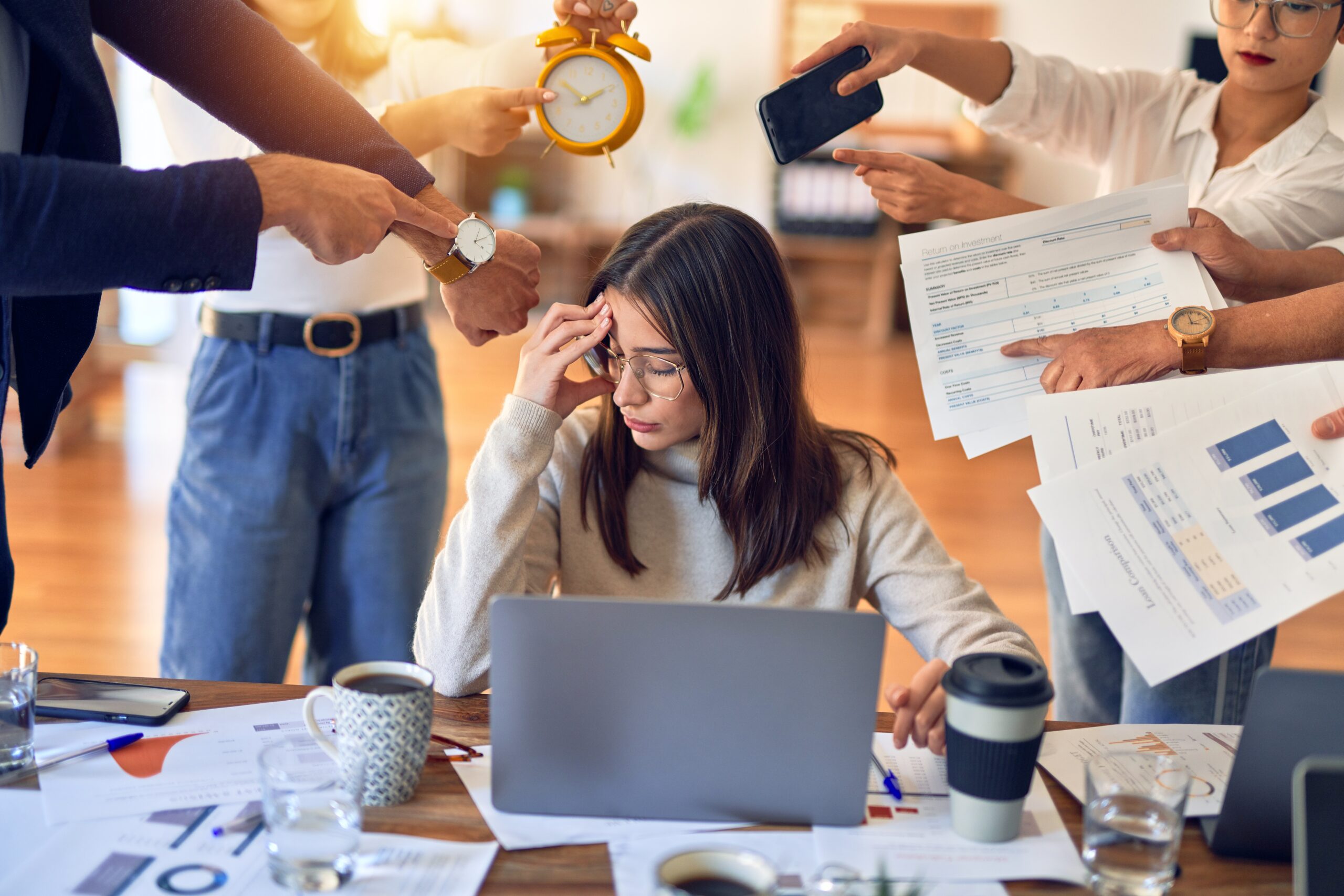 Woman sitting at desk surrounded by team members bombarding her with request. Executive burnout is rising fast. Discover neuroscience-based recovery steps to reset your energy, reclaim clarity, and rebuild sustainable high performance.