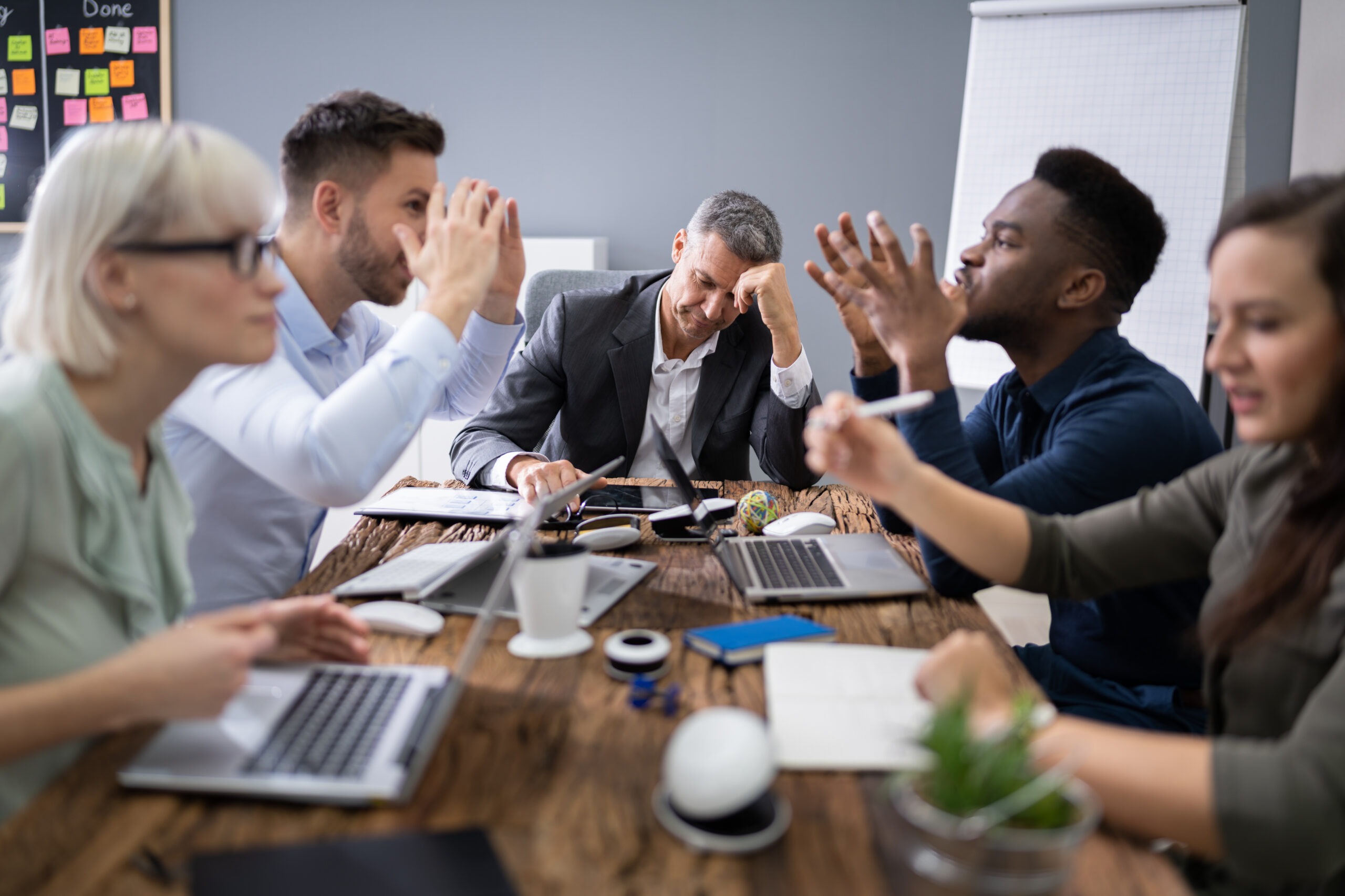A group of diverse professionals sitting at a table in a meeting frustrated. Using Conflict to Fuel Growth