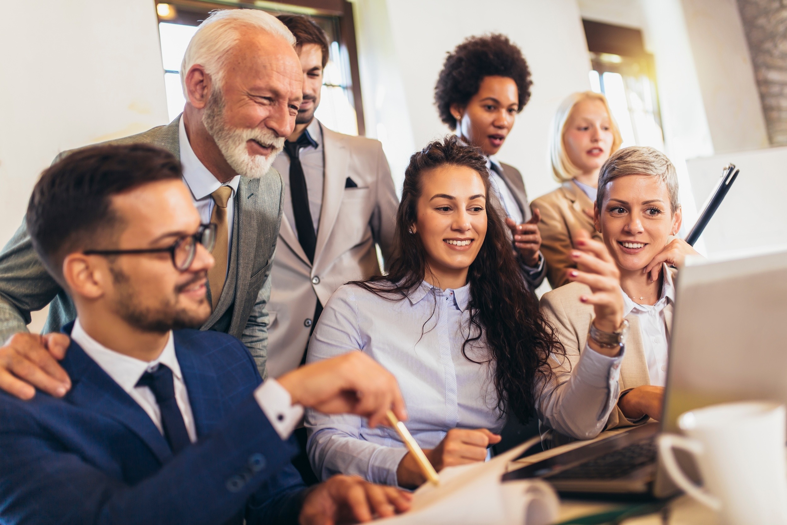 Image of professionals working together smiling sitting and standing looking at computer. Genuine Connection: The Most Underrated Asset in Corporate Leadership